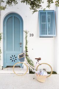 Blue arched door and shuttered window on a white wall, with a bicycle and basket parked outside