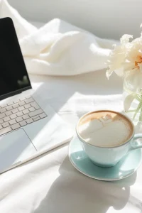 Sunlit desk with a laptop, a latte in a pale blue cup and cream flowers